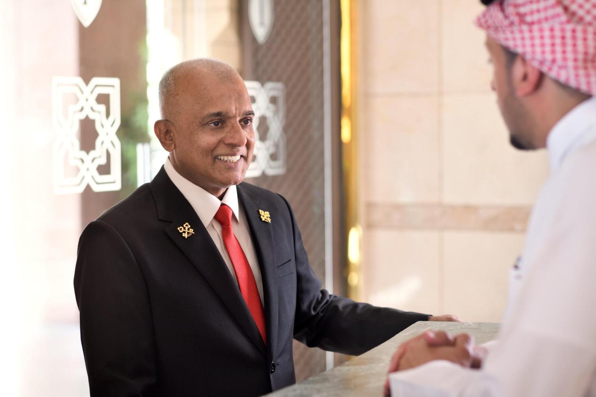 Intercontinental Dar Al Hijra Madinah, An Ihg Hotel Medina Exterior photo The photo shows two men engaged in conversation at a hotel reception desk. One man is wearing a dark suit with a red tie and has a welcoming smile. The other man is dressed in traditional attire, possibly a thobe, and a headscarf. The setting appears