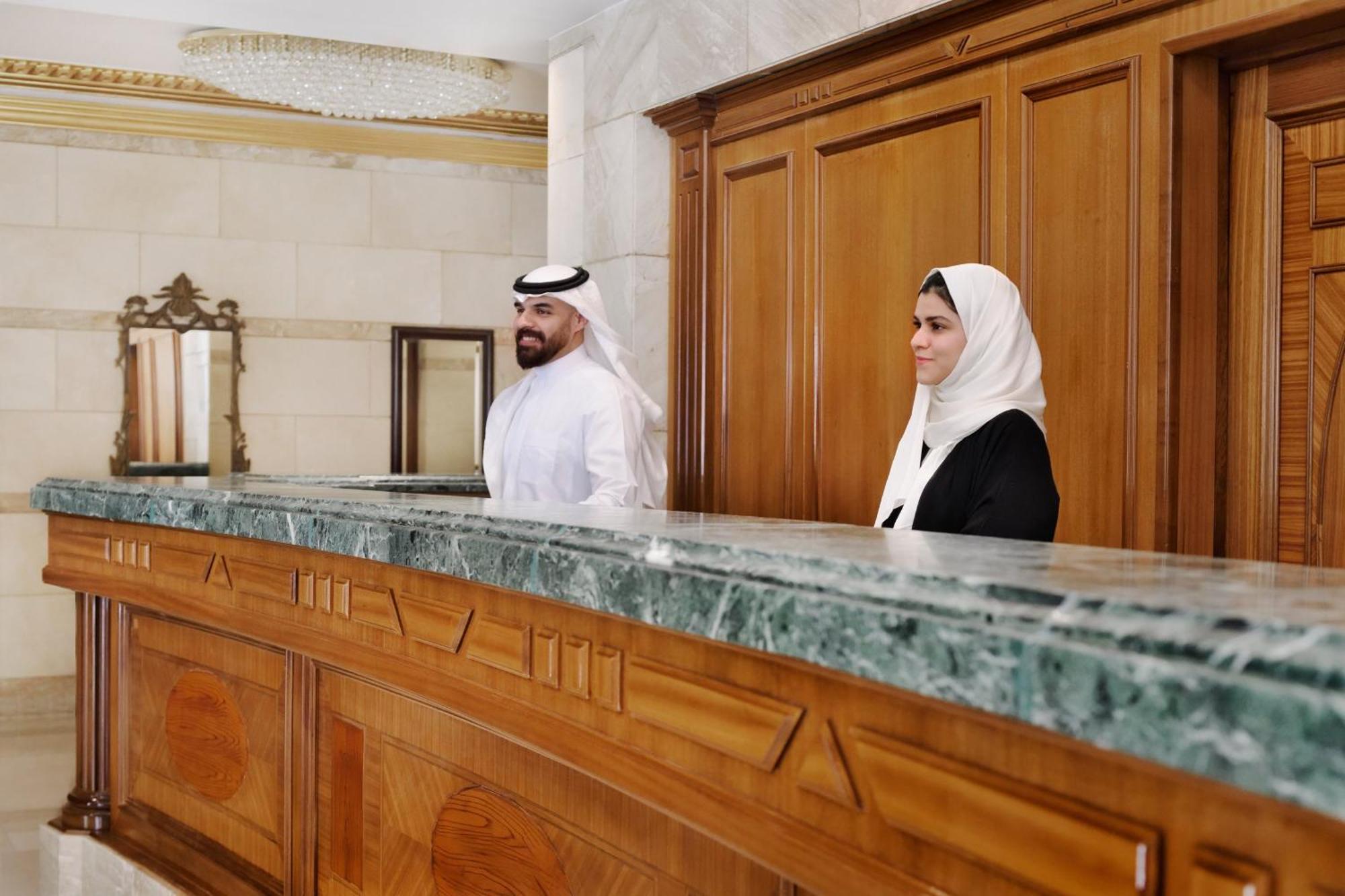 Intercontinental Dar Al Hijra Madinah, An Ihg Hotel Medina Exterior photo The photo shows two individuals standing behind a reception or service desk. The desk appears to be made of wood with a green marble top. One of the individuals is wearing a traditional outfit and a headscarf, while the other is dressed in a black ou