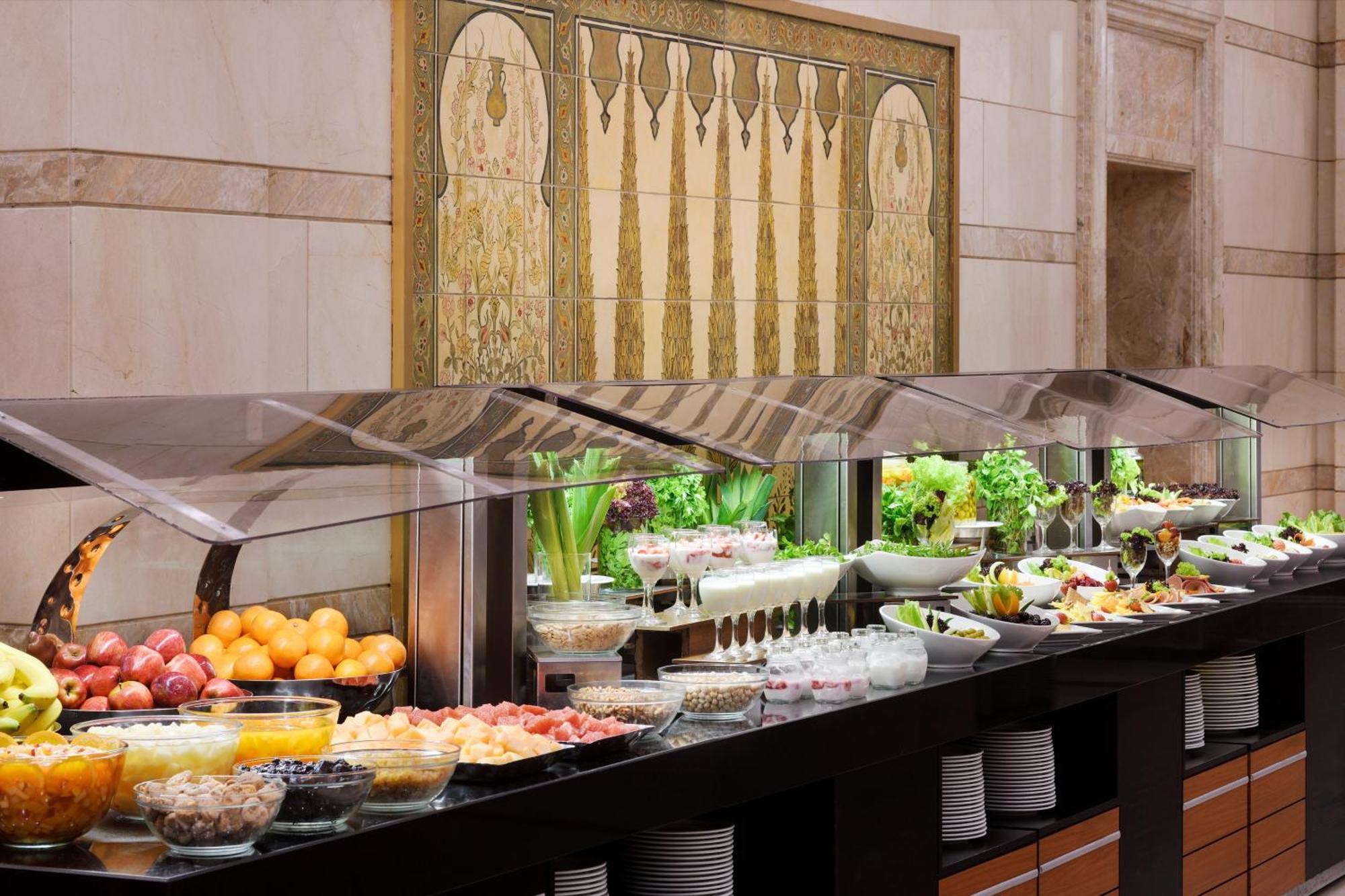 Intercontinental Dar Al Hijra Madinah, An Ihg Hotel Medina Exterior photo The photo shows a buffet setup featuring a variety of fresh fruits, salads, and other dishes. There are several glass display cases filled with colorful and neatly arranged items, including apples, oranges, and bowls of different salads and garnishes