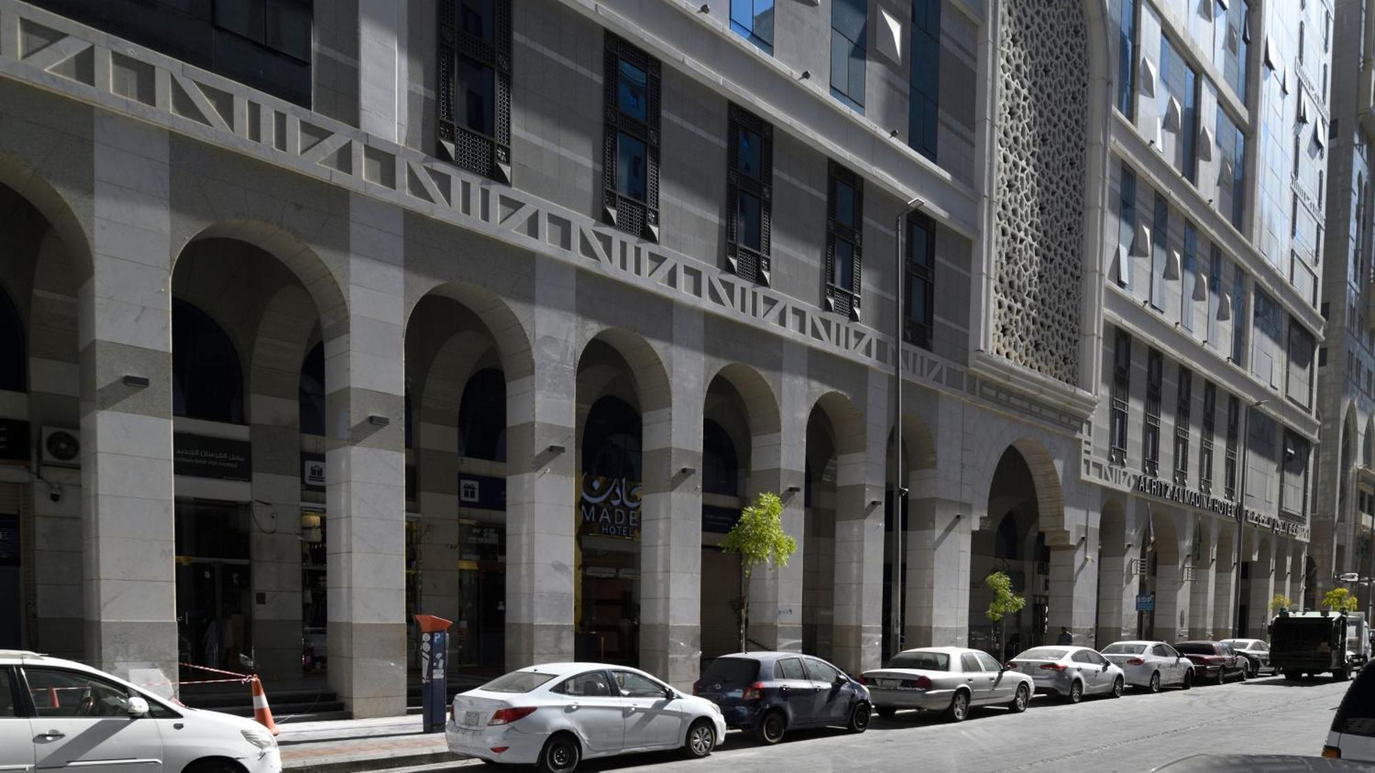 Intercontinental Dar Al Hijra Madinah, An Ihg Hotel Medina Exterior photo The photo shows a street scene featuring a modern architectural building with a façade that includes arched columns. The building has a combination of gray and light-colored materials, with rectangular windows. There are several parked cars along the